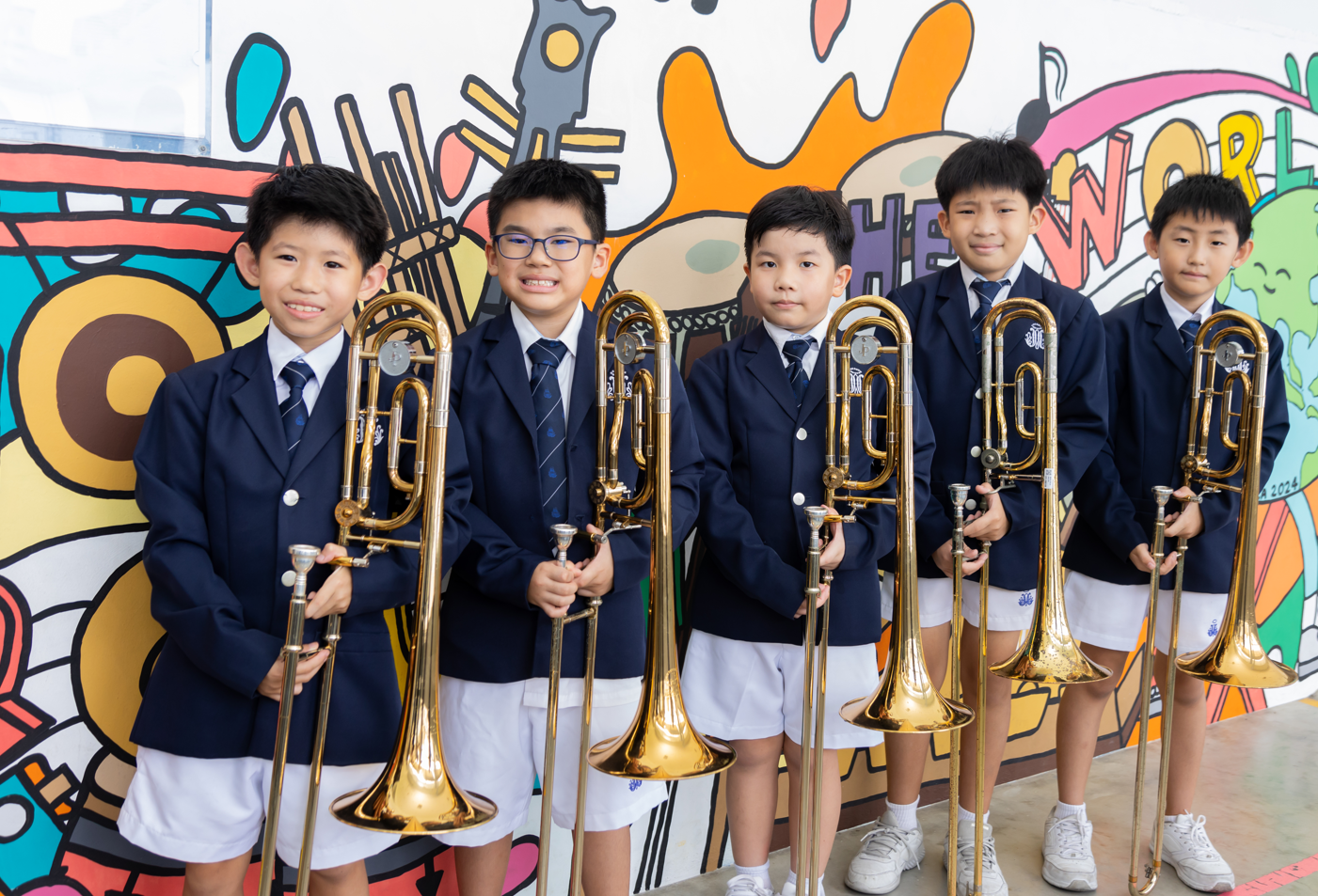 Young boy in school uniform playing a large brass tuba with other student musicians seated behind him.